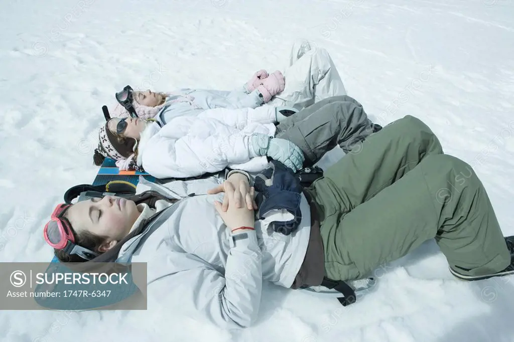 Three sisters lying on snow with heads resting on snowboard