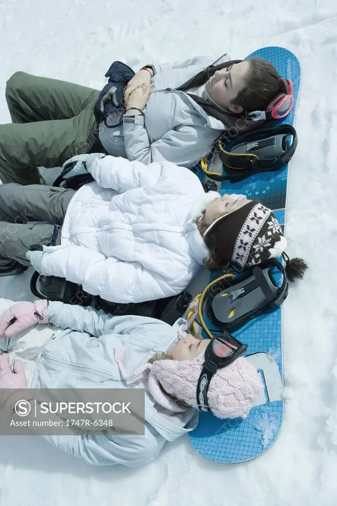 Three sisters lying on snow with heads resting on snowboard
