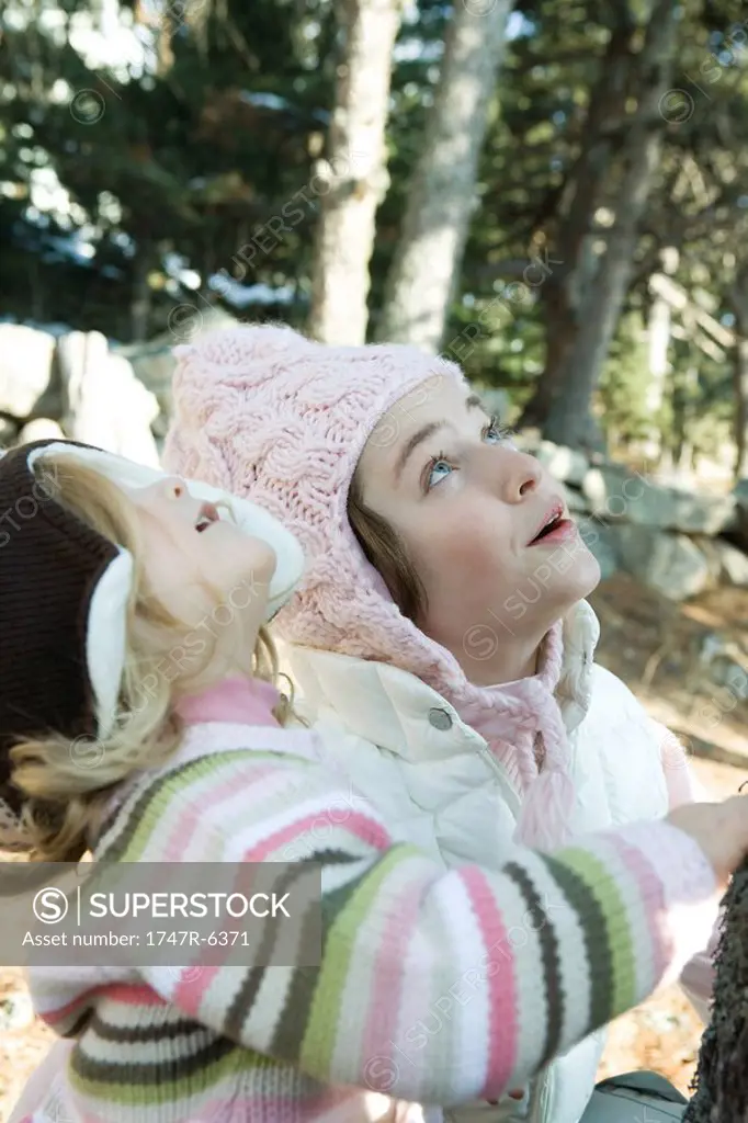 Teen girl and toddler, in woods, looking up together