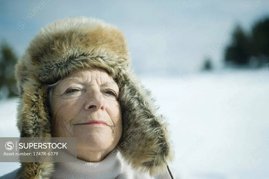 Senior woman standing in snowy landscape, eyes closed, smiling, head and shoulders