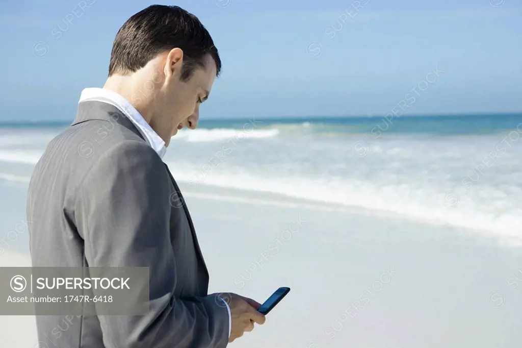 Businessman on beach, using cell phone