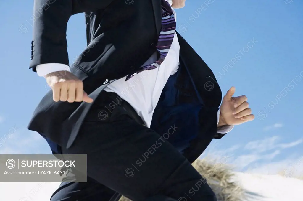 Businessman running, sand dune in background, cropped view of mid section