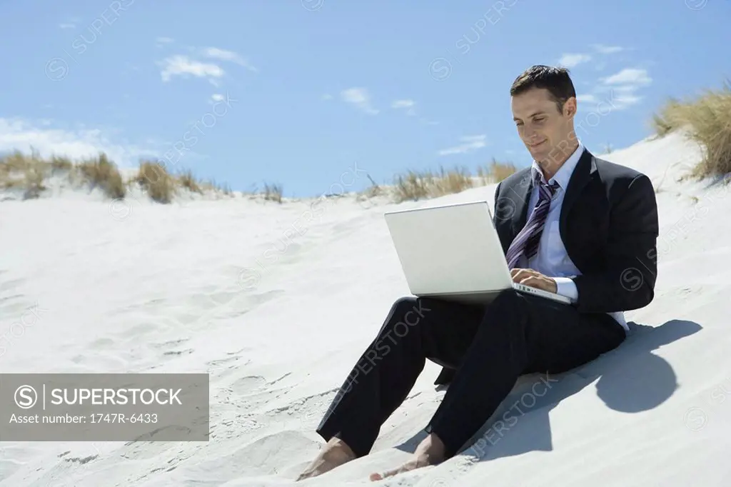 Businessman sitting on sand dune, using laptop