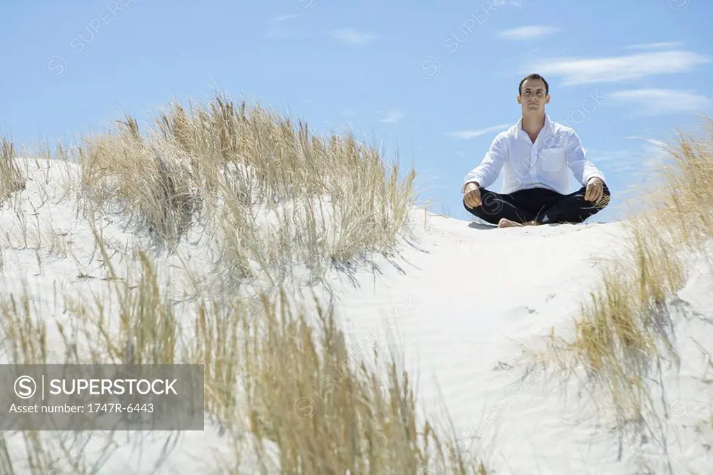 Businessman sitting on sand dune, indian style
