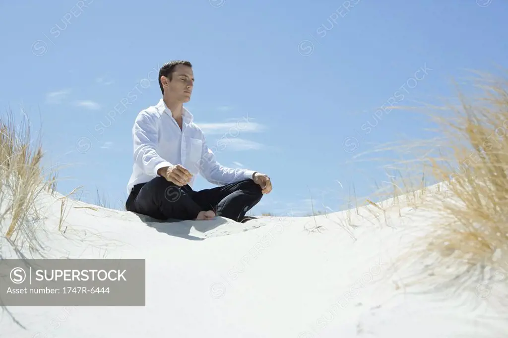 Businessman sitting on sand dune, meditating