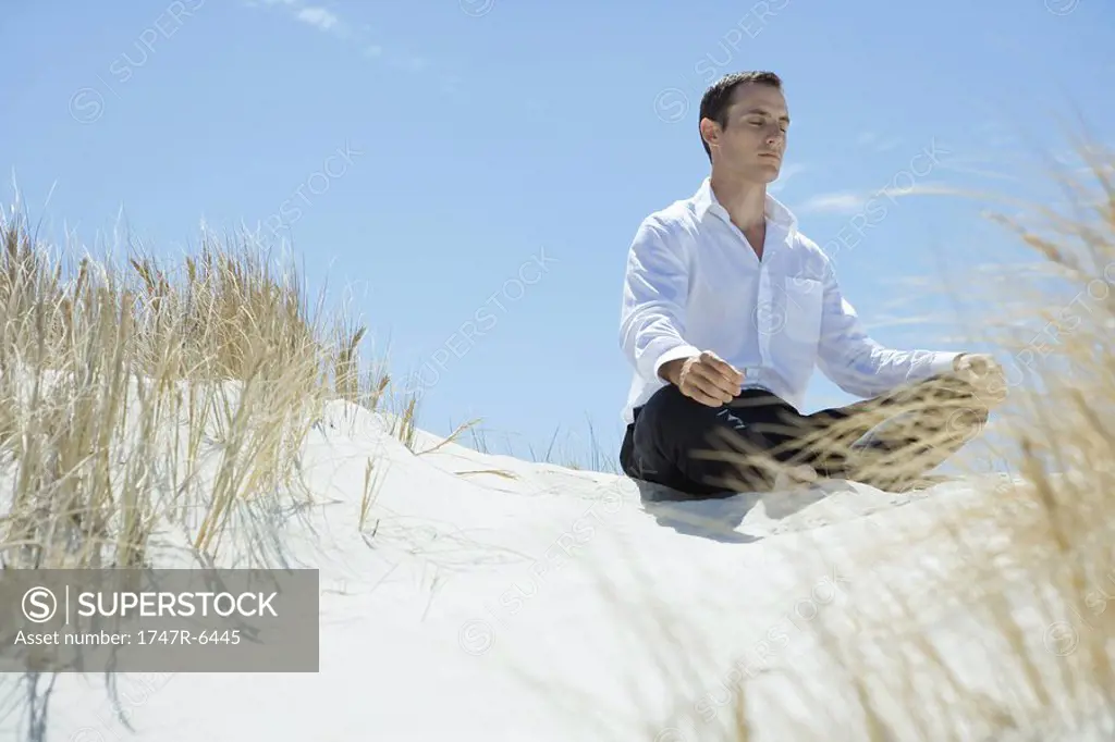 Businessman sitting on sand dune, meditating