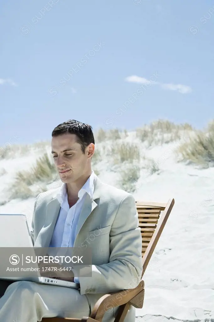 Businessman sitting in deck chair at beach, using laptop