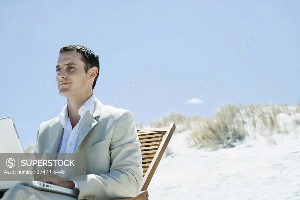 Businessman sitting in deck chair at beach, using laptop