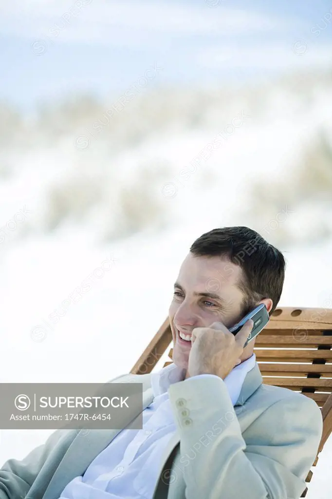 Businessman sitting in deck chair at beach, using cell phone