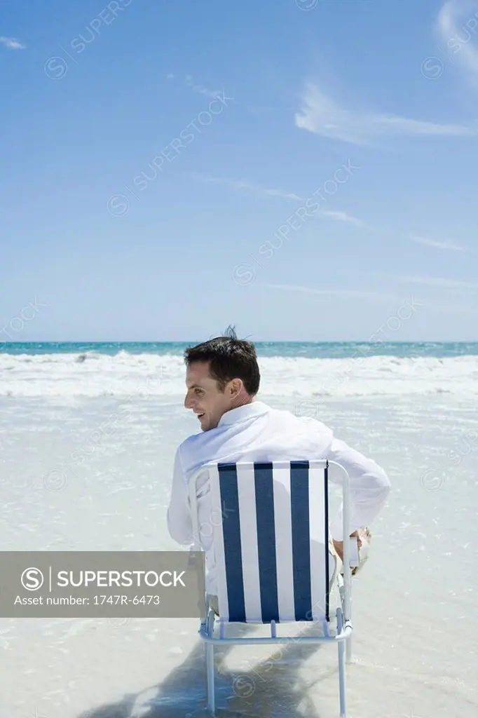 Man sitting in folding chair on beach, rear view