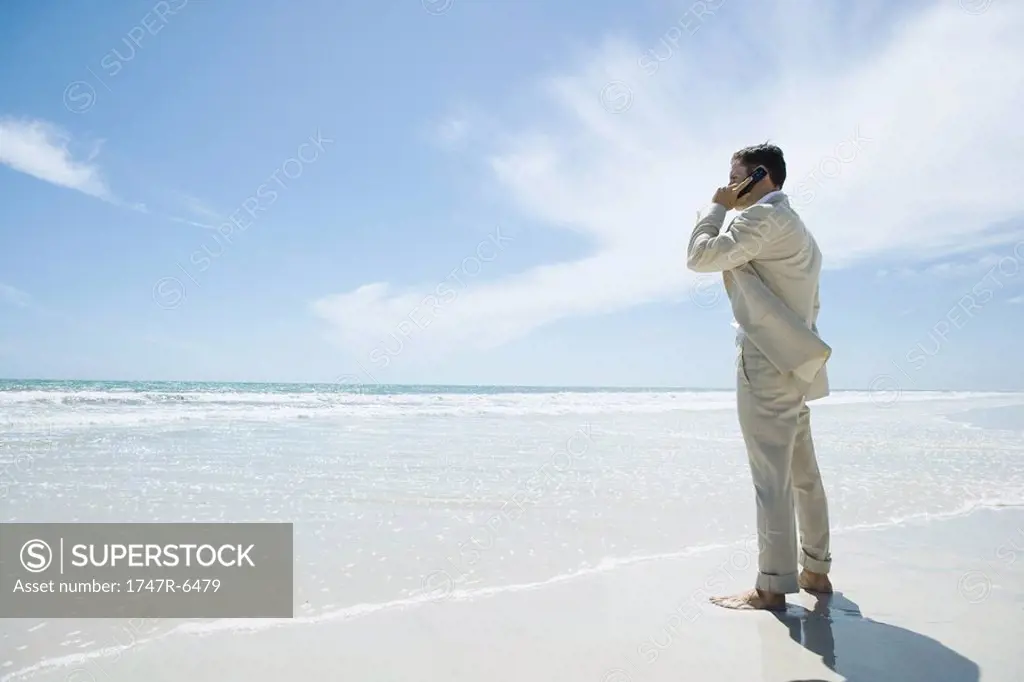 Businessman standing barefoot on beach, using cell phone
