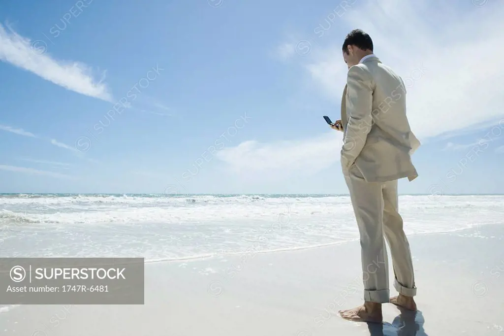 Businessman standing barefoot on beach, holding cell phone
