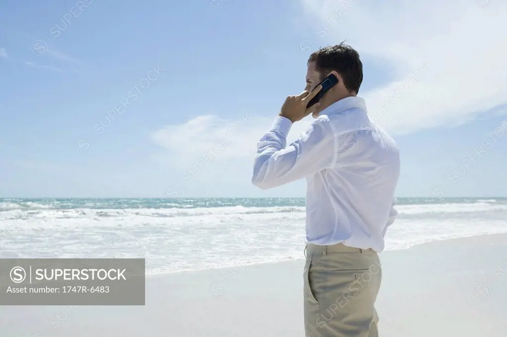 Businessman using cell phone on beach, side view