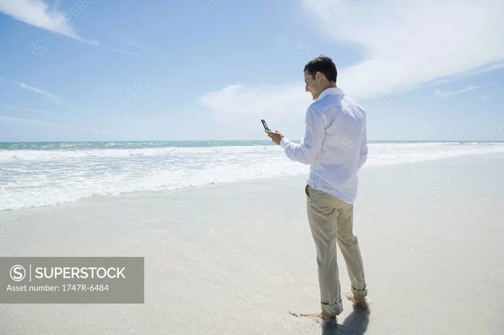 Businessman standing barefoot on beach, holding up cell phone