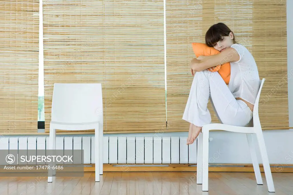Young woman sitting in chair, hugging cushion
