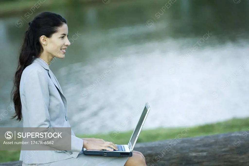 Woman using laptop, lake in background