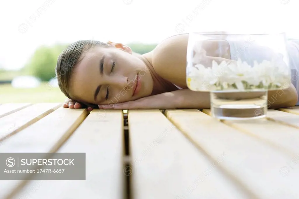 Woman lying on deck, next to container of floating flowers