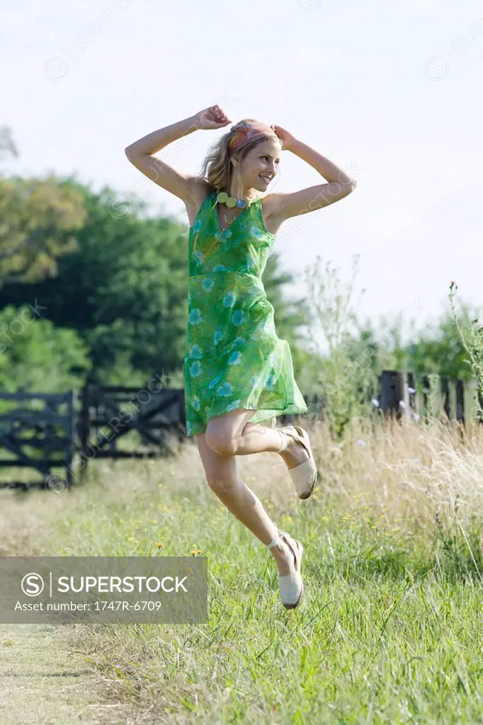 Young woman in sundress jumping in rural field