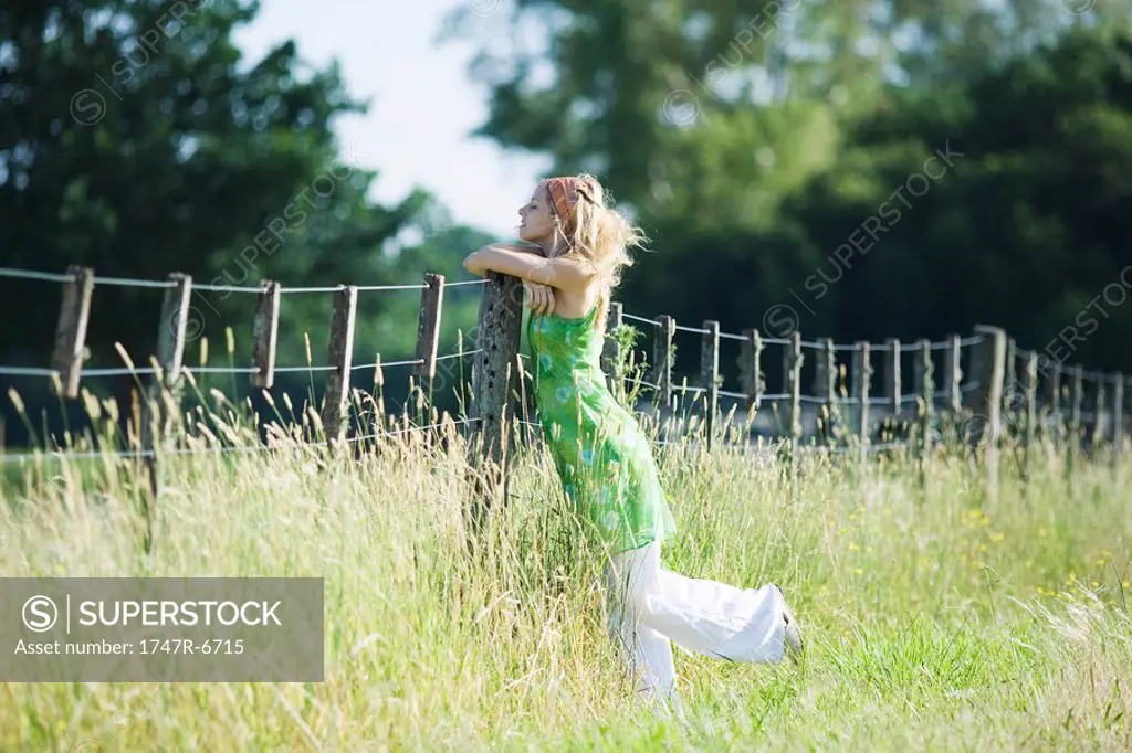 Young woman leaning against rural fence with eyes closed