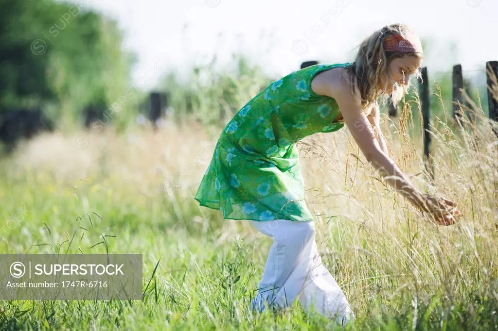 Young woman bending over to touch tall grass in rural field