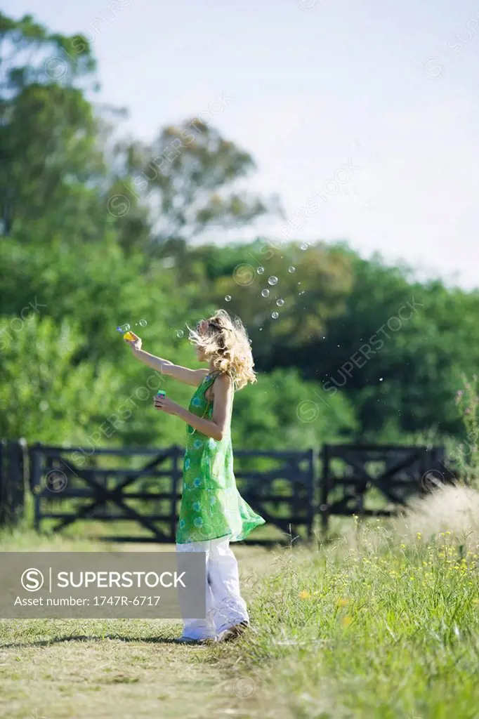 Woman blowing bubbles on rural path, side view