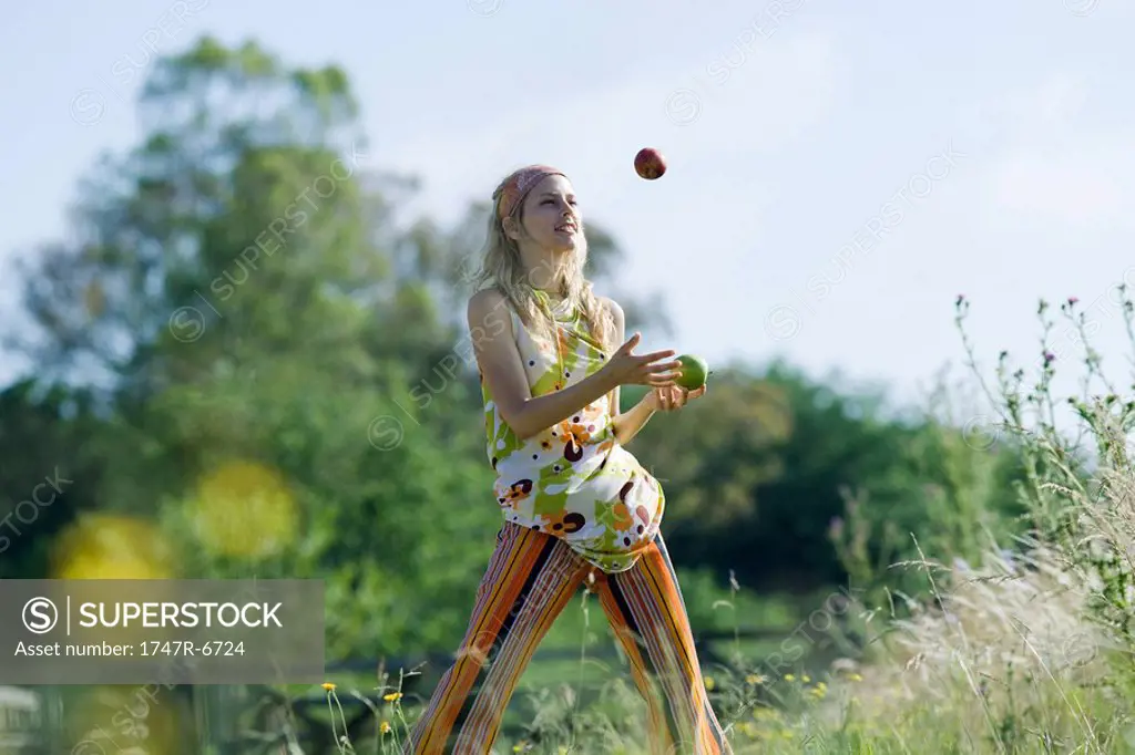 Young woman standing in field, juggling apples