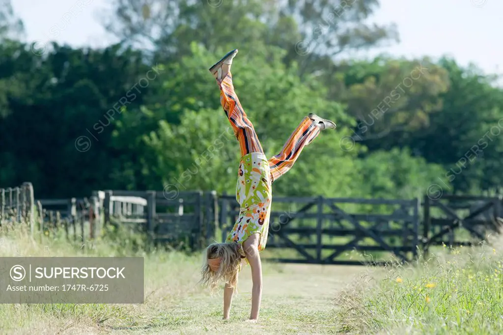 Young woman doing handstand in rural field