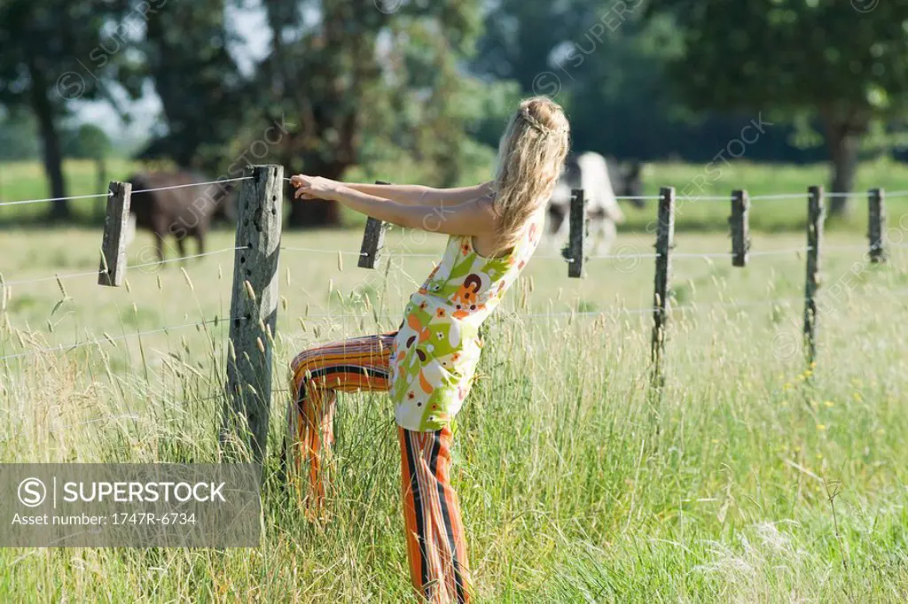 Young woman holding on to rural fence, side view