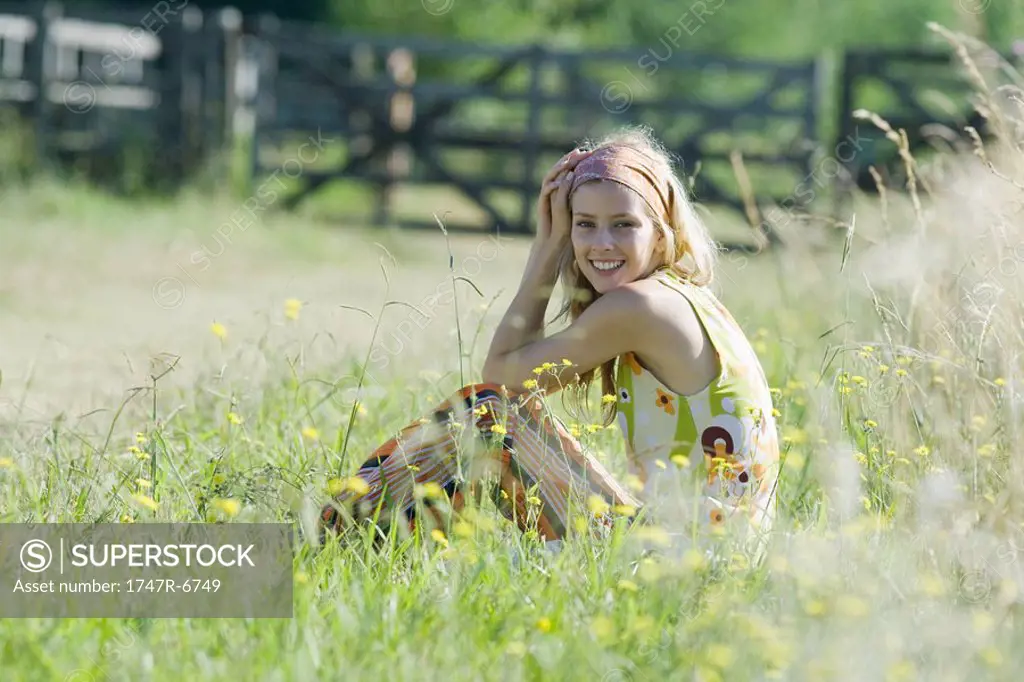Young woman sitting in tall grass with knees up, smiling at camera