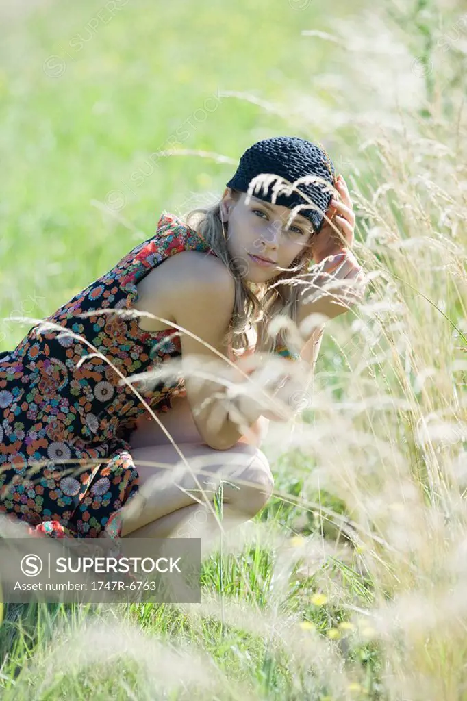 Young woman crouching in tall grass, smiling at camera