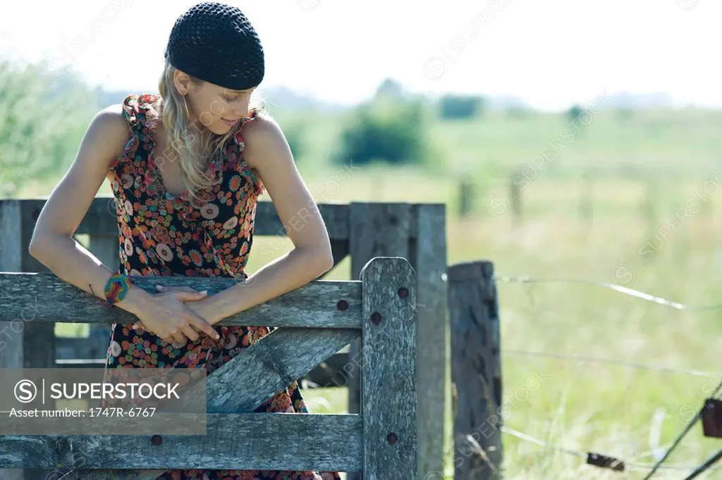 Young woman holding on to wooden fence, looking away