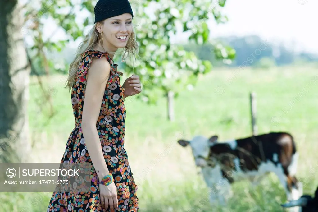 Young woman walking toward cow, smiling, looking away