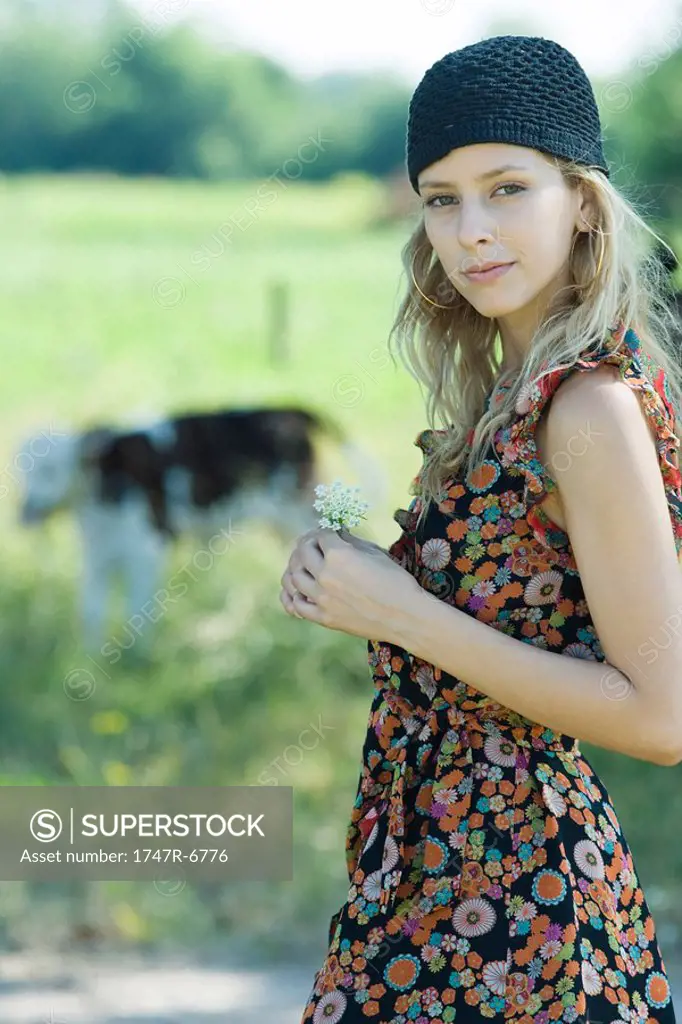 Young woman holding flower in rural setting, smiling at camera