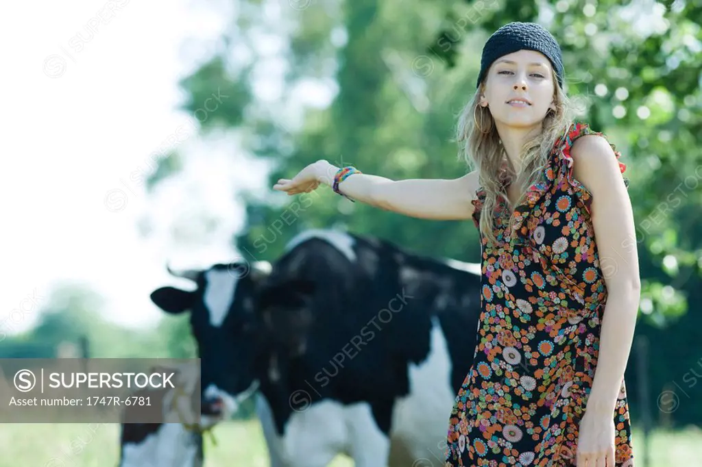 Young woman standing in front of cows, arm outstretched behind her, smiling at camera