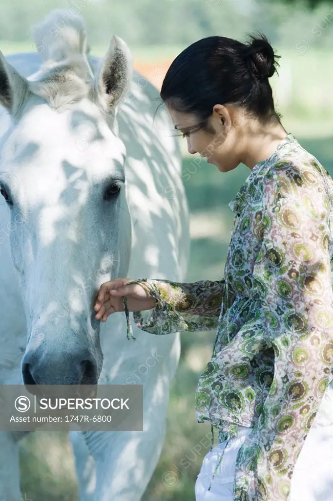 Young woman touching horse, side view