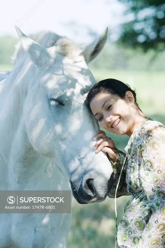 Young woman leaning her head against horse, smiling