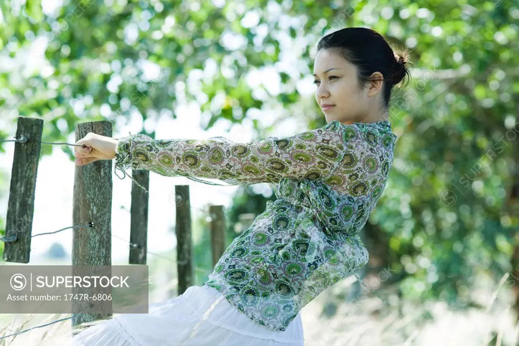 Young woman holding on to rural fence, leaning back