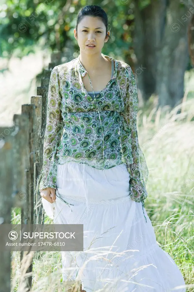 Young woman walking beside rural fence, looking at camera