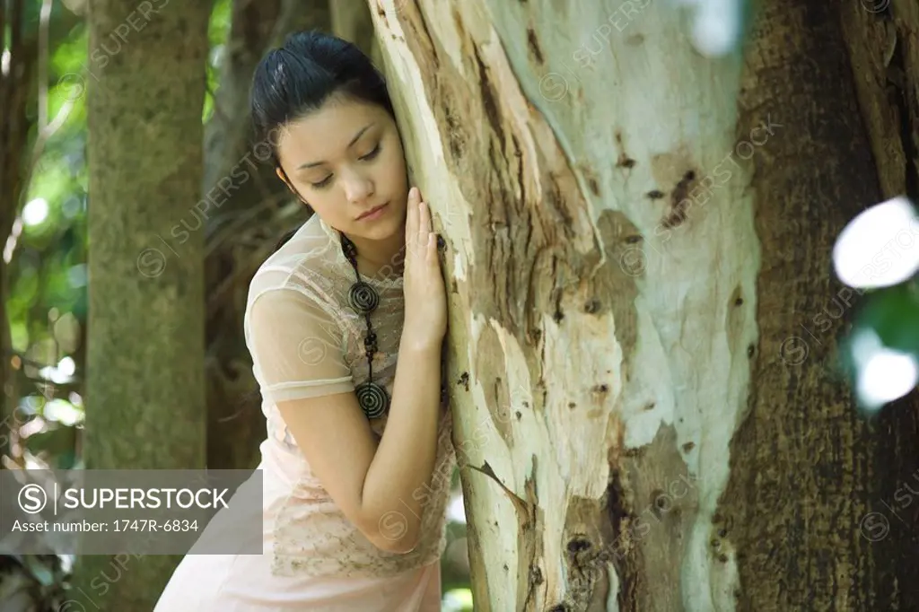 Young woman leaning head against tree trunk, eyes closed