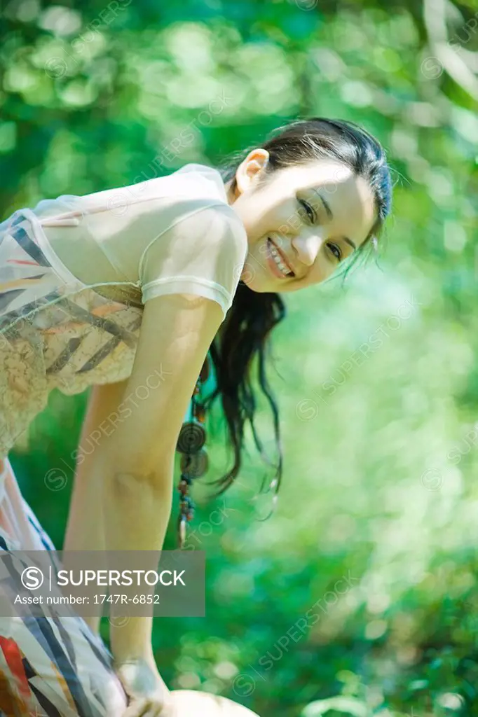 Young woman bending over outdoors, smiling at camera