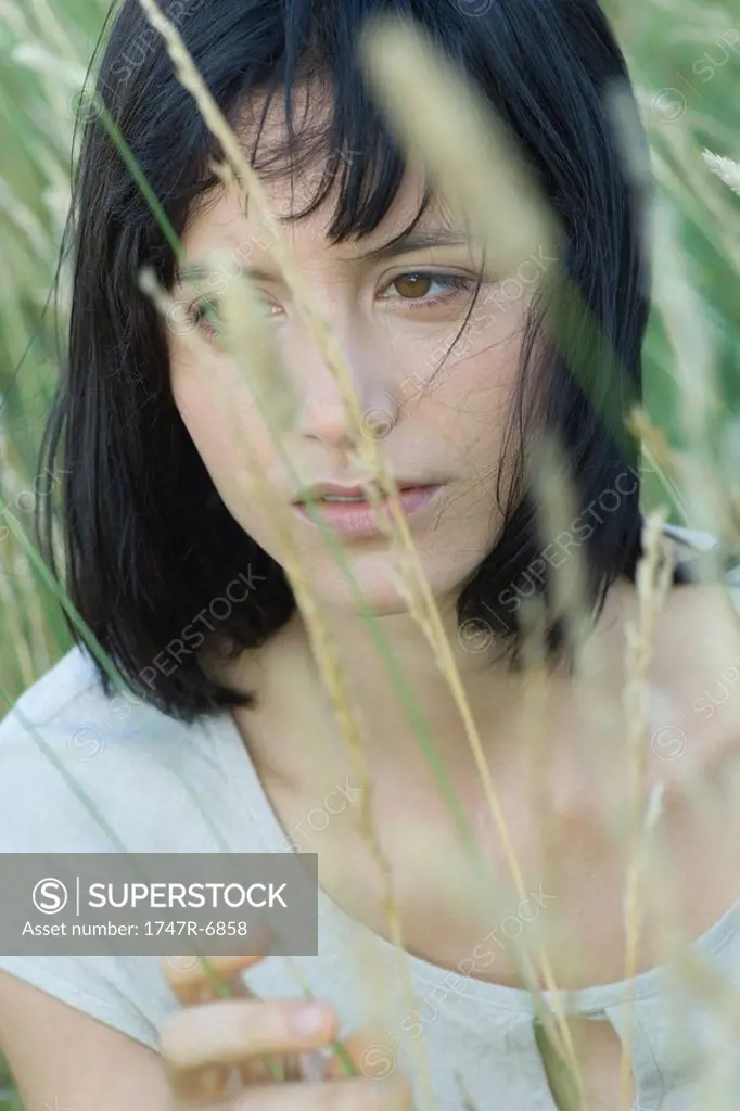 Young woman in tall grass, looking away, portrait