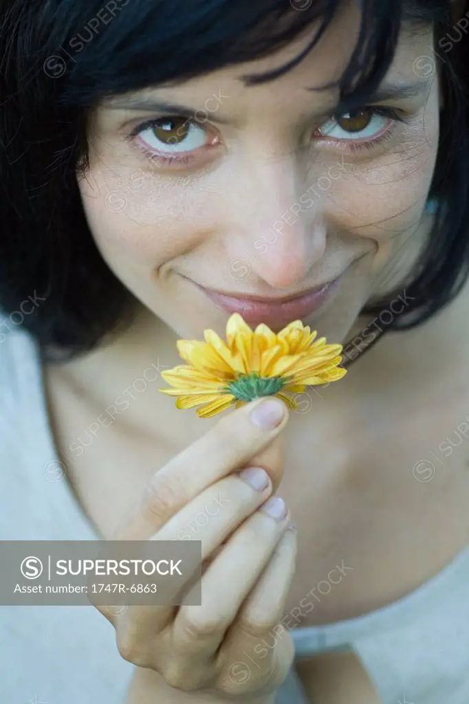 Young woman smelling flower, smiling at camera, cropped, close-up