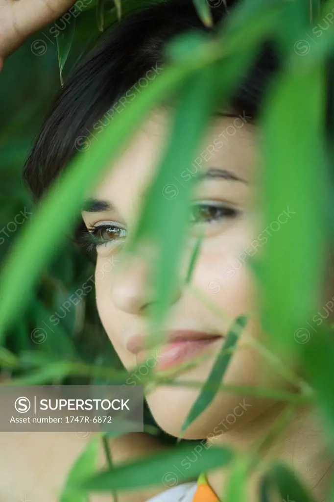 Young woman among foliage, smiling, looking away, close-up