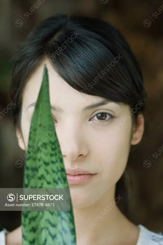 Young woman looking at camera with leaf covering one eye, portrait