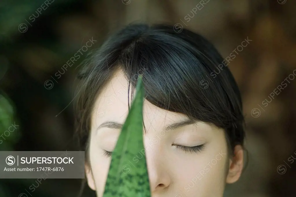 Young woman behind leaf, eyes closed, cropped portrait