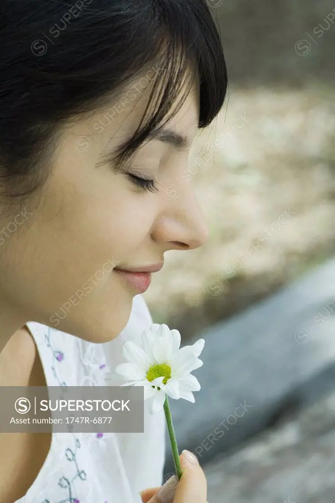 Young woman smelling flower with eyes closed, profile