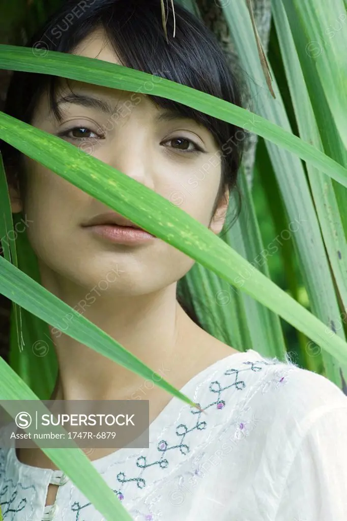 Young woman looking through palm leaf at camera, portrait