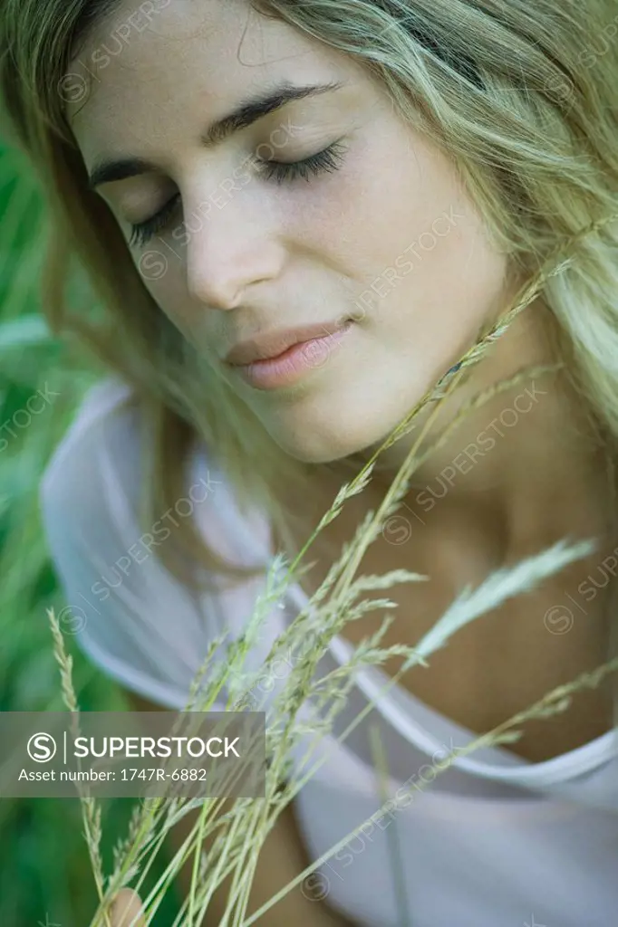 Young woman holding tall grass, eyes closed, close-up