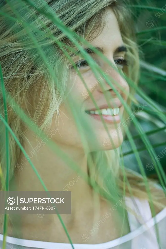 Young woman among foliage, looking away, smiling