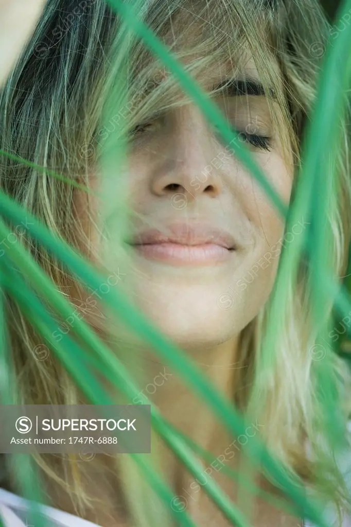 Young woman among foliage, hair in face, eyes closed, close-up